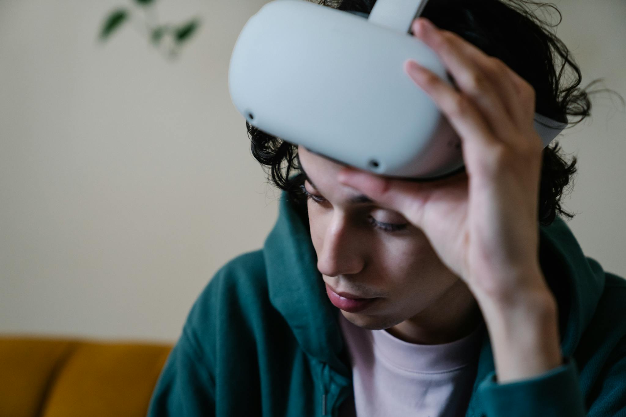 Crop male holding hand on modern VR goggles for experiencing virtual space while sitting on couch